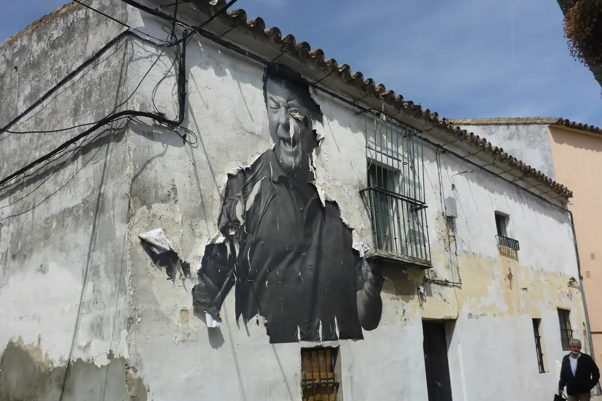 A large black-and-white portrait of a laughing flamenco singer pasted on the peeling whitewashed wall of a house in Jerez